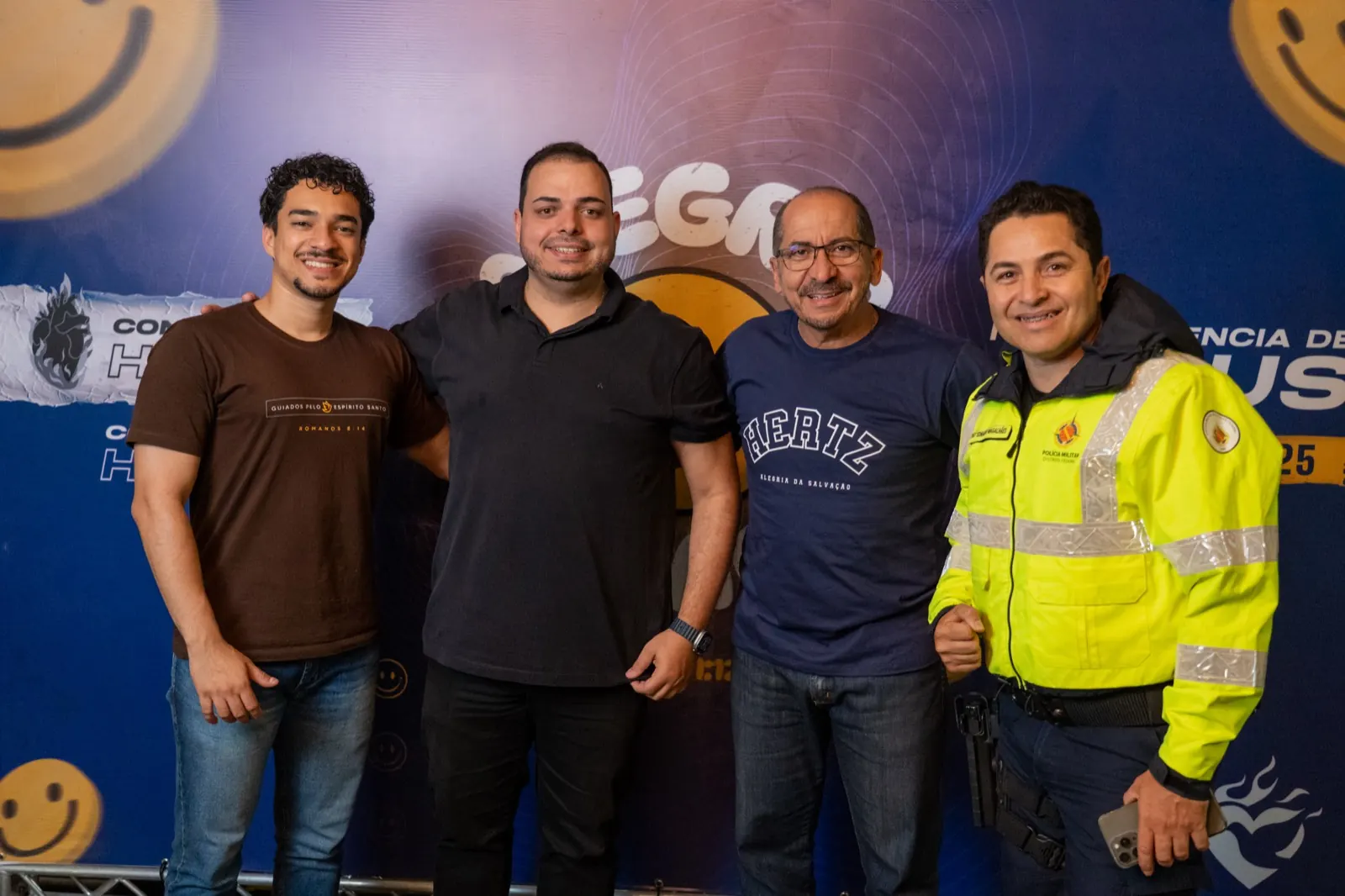 Quatro homens sorrindo juntos diante do painel da Conferência Hertz 2025