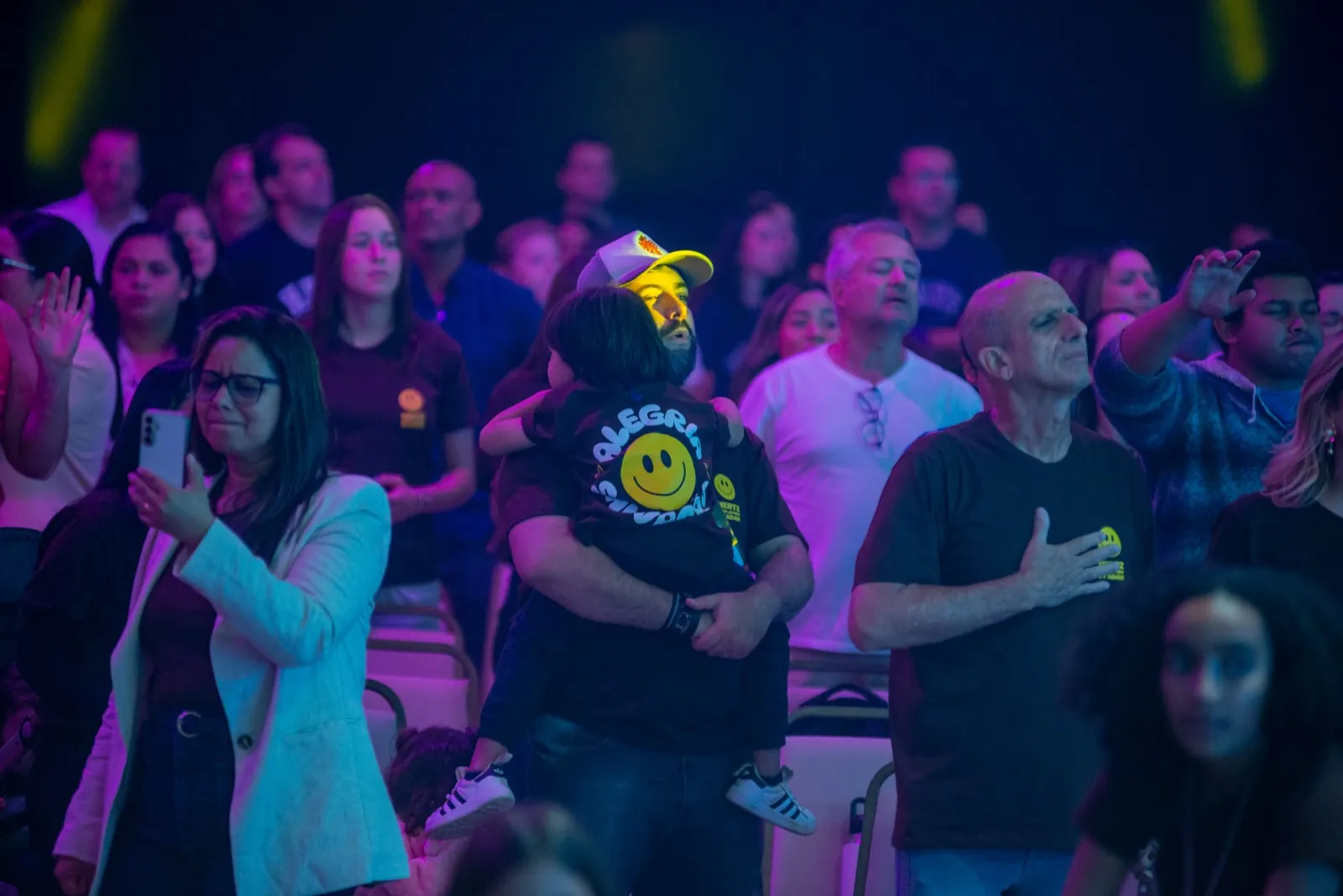 Homem com boné carregando uma criança no colo durante o louvor