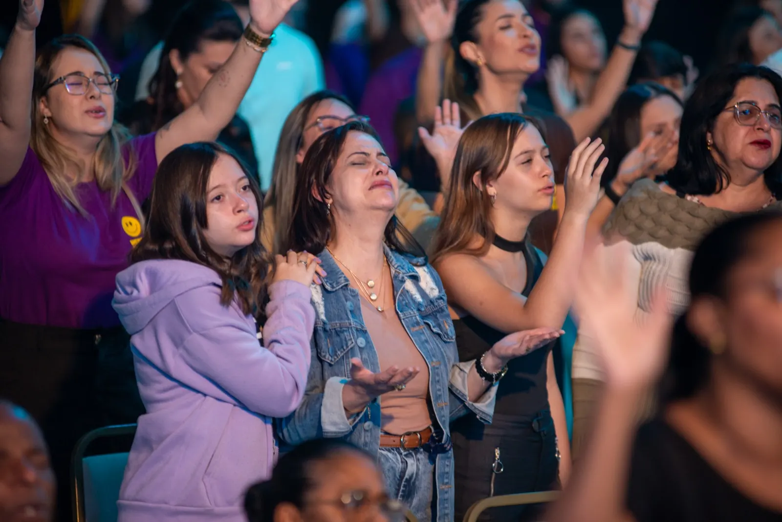 Mulheres e jovens de mãos erguidas, orando durante o louvor