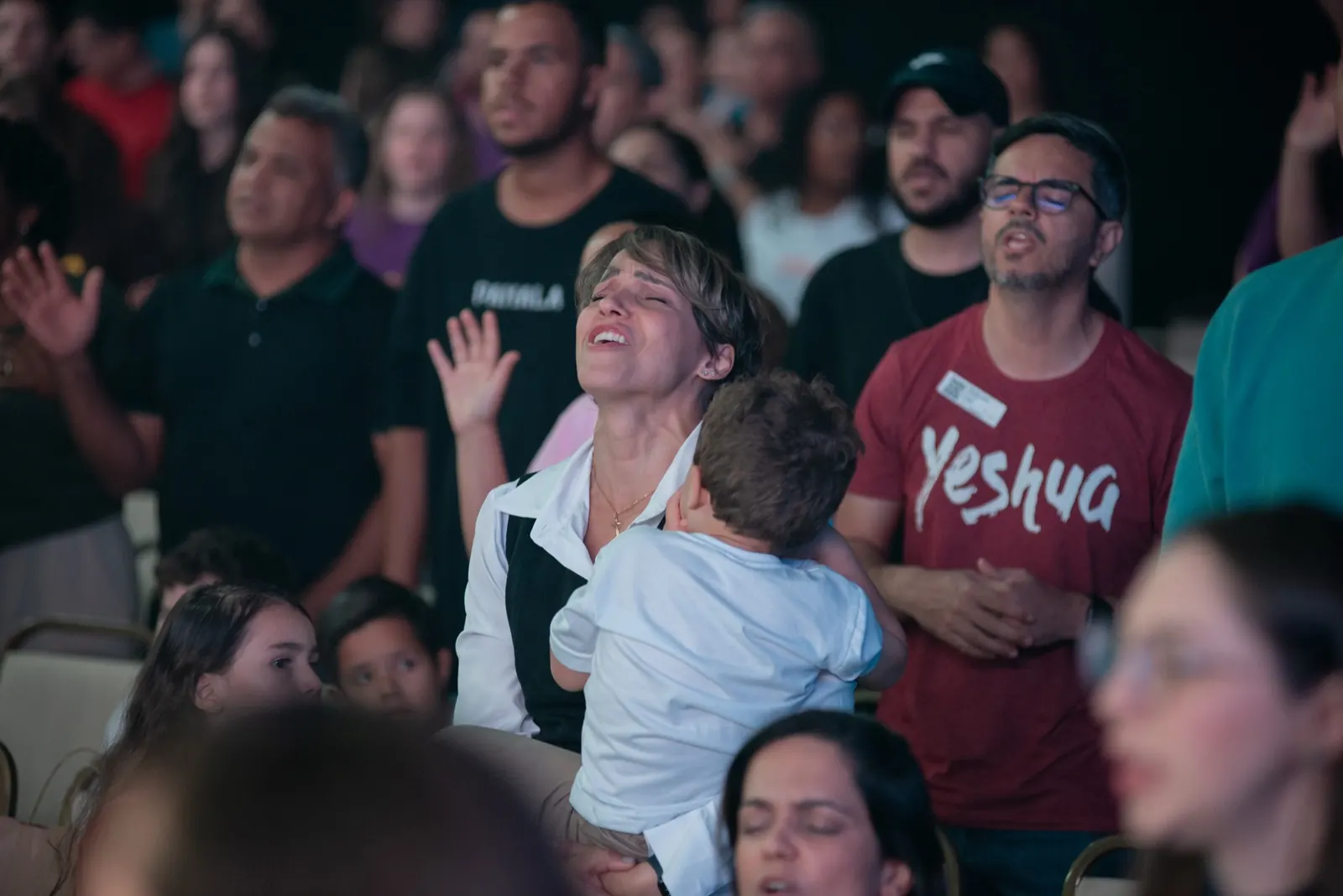 Mulher cantando com os olhos fechados, com uma criança no colo
