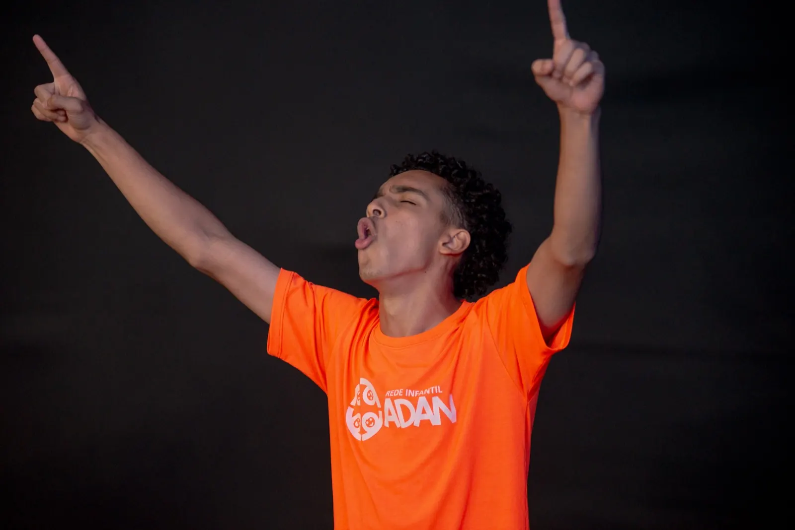 Jovem de camiseta laranja da Rede Infantil Adan, com os dois indicadores apontados para cima